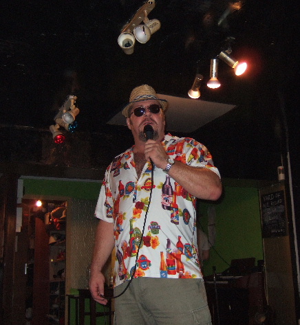 A man in a hawainan shirt in sungalsses inside a dark club.